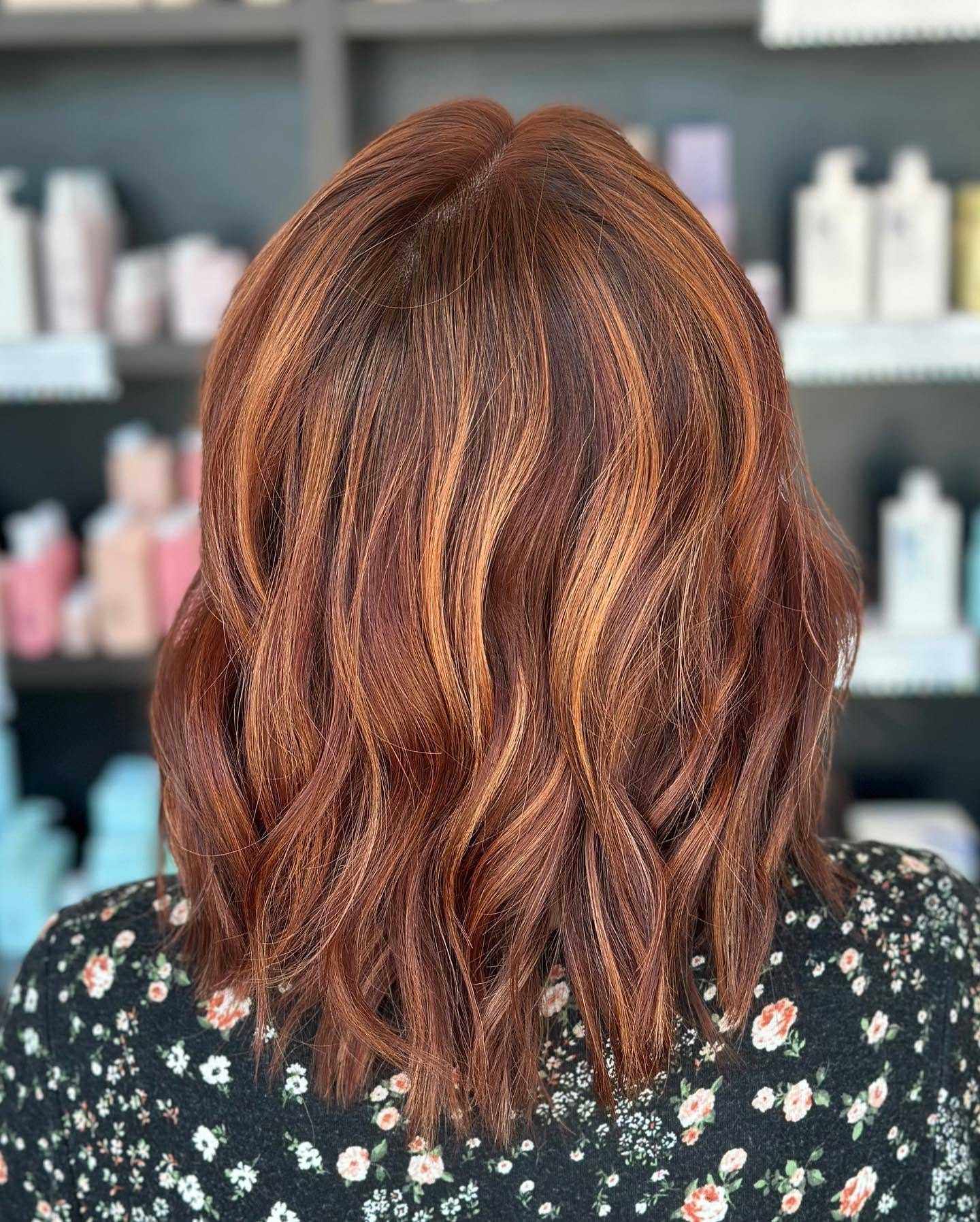 Bob haircut with copper and blonde highlights, styled in loose waves, in front of salon shelves.