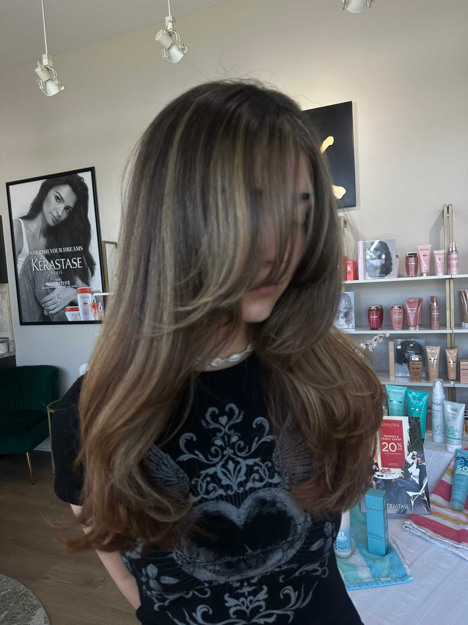 Hair salon interior with a focus on a client with styled long hair and salon products displayed.