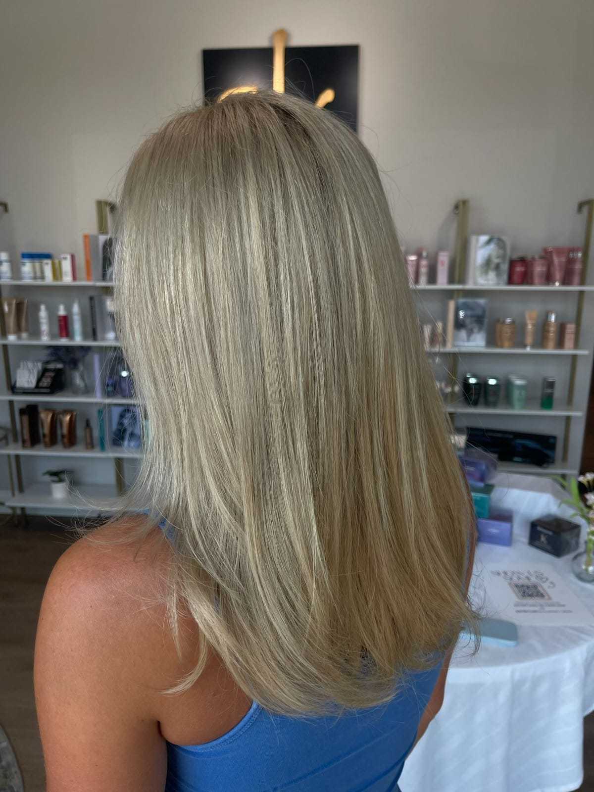Blonde woman with straight hair in a salon, surrounded by beauty products.